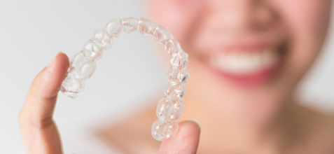 Woman smiling while holding clear aligners